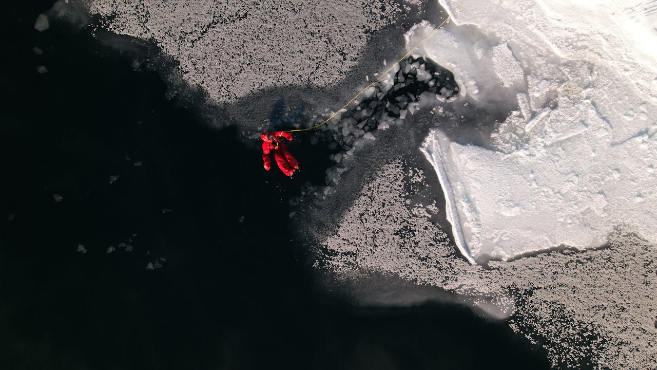 gallery-01 Drone photo of a person in a red suit on Arctic ice, showcasing stark contrasts.
